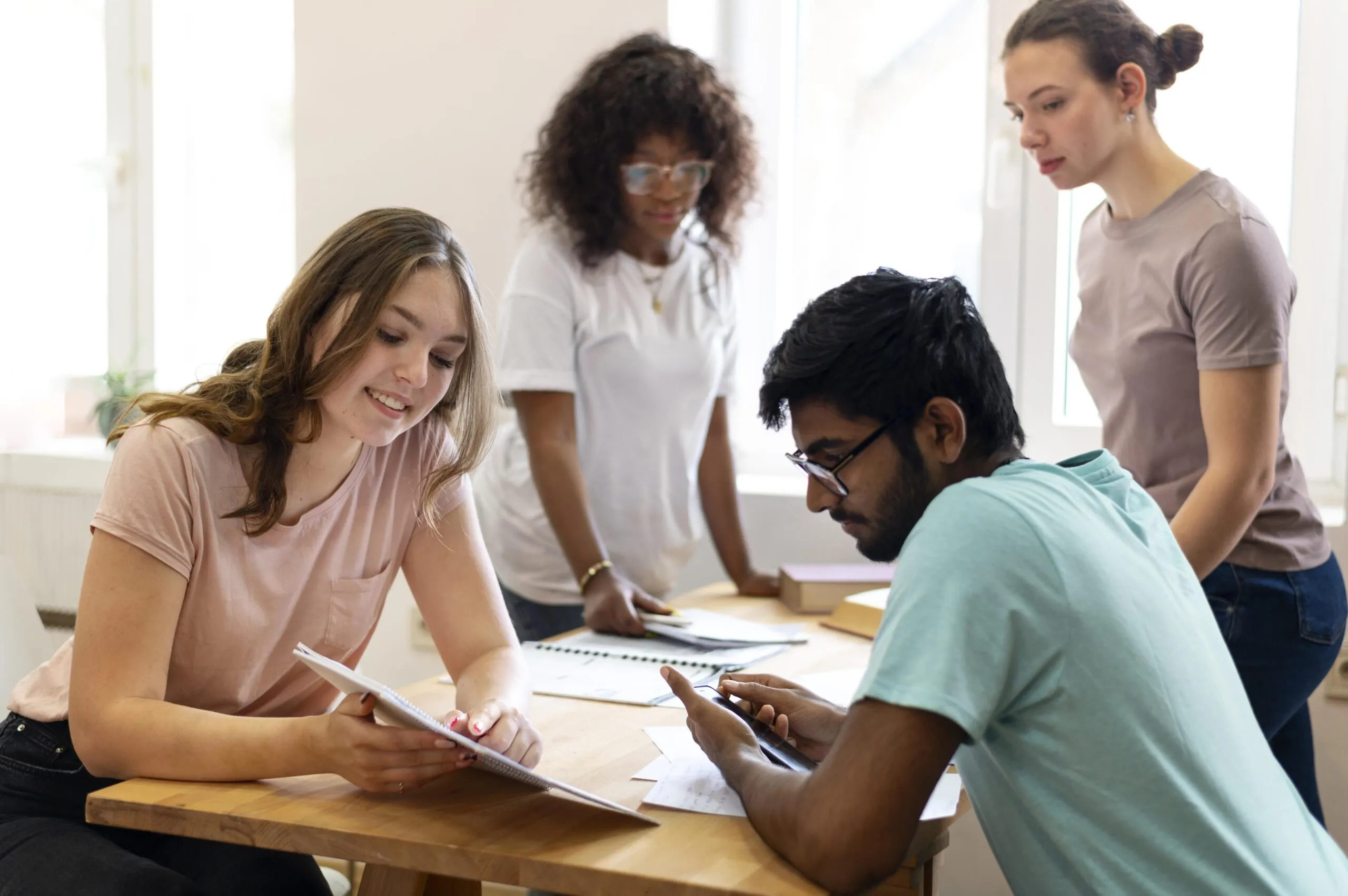 3 jovens do sexo feminino e 1 jovem do sexo masculino ao redor de uma mesa de estudos, com cadernos estudando - Remetendo ao tema do artigo preparação para TRT-RN  Edital do Concurso Público .