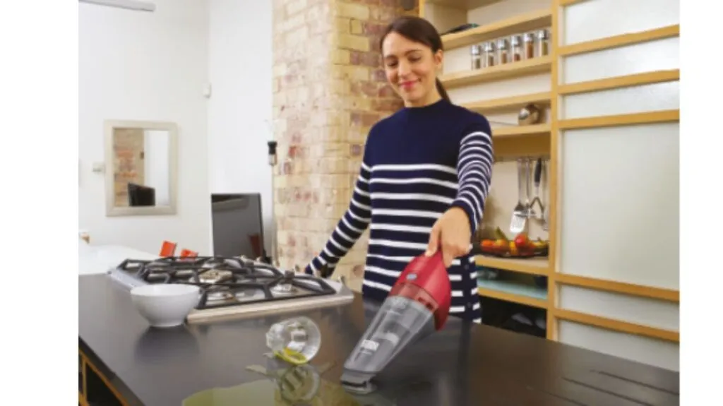 Mulher  na bancada da cozinha aspirando suco derramado com um Black Decker Aspirador de Pó e Àgua Portátil cor vermelha.